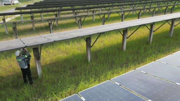 Lavoratore ingegnere controllando un pannello solare e camminando in fattoria solare. ingegneri ispeziona la costruzione del pannello di celle solari. Il volo dei droni sorvola il campo dei pannelli solari energie alternative rinnovabili verdi. - Filmati, video
