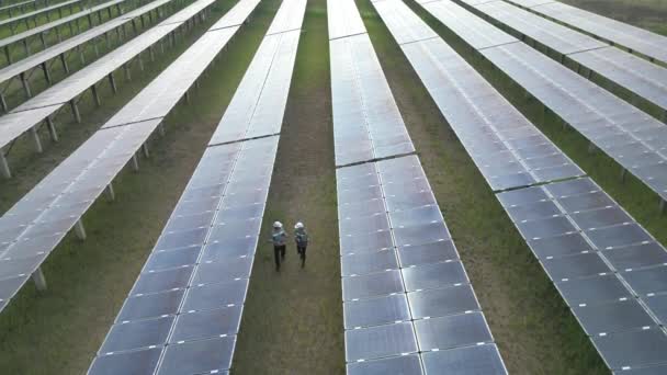 Bovenaanzicht van ingenieurs die een zonnepaneel controleren en in een zonnepark lopen. ingenieurs inspecteert de bouw van zonnecellen paneel. Drone vlucht vliegen over zonnepanelen veld hernieuwbare groene energie. - Video