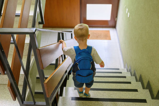 Back view of little boy with blond hair in casual clothes with backpack standing on stairs before going to kindergarten in the morning. family concept - Fotoğraf, Görsel