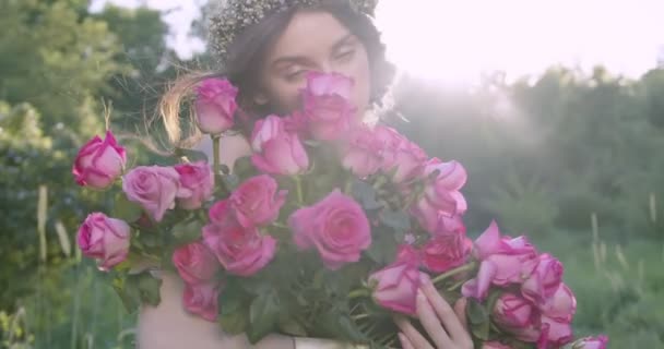 A young girl with a wreath of flowers holds a large bouquet of roses among the spring garden. Slow motion - Metraje, vídeo