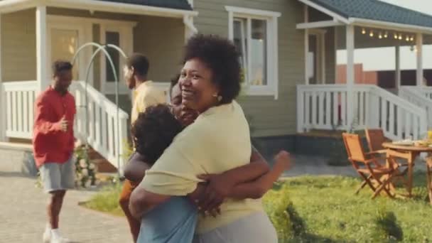 Orta ölçekli, neşeli, siyahi bir kadın, genç yeğenlerini selamlıyor ve kucaklıyor. Bu arada evin bahçesindeki yeşil çimenlikte aile yemeği için bir araya geliyorlar. - Video, Çekim