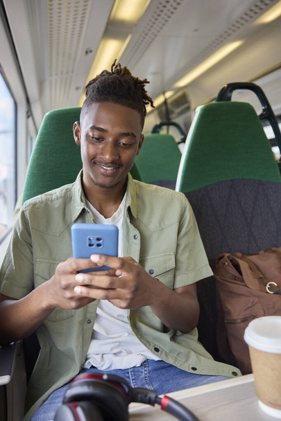 Young Man Commuting To Work On Train Sitting  On Train Looking At Mobile Phone For Travel Information Or Social Media - Photo, image