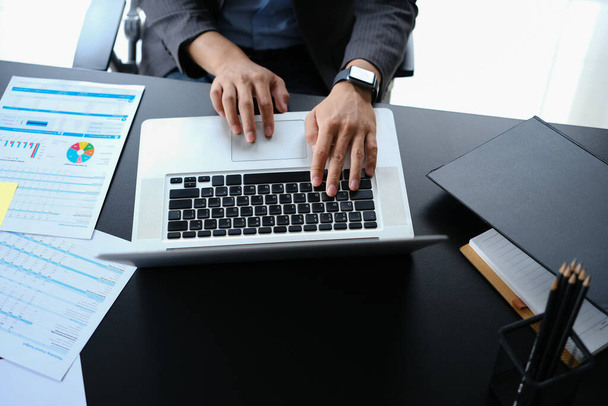 Vista superior de manos de hombre de negocios escribiendo en el ordenador portátil, trabajando con gráfico financiero, documento estadístico en el lugar de trabajo. - Foto, imagen