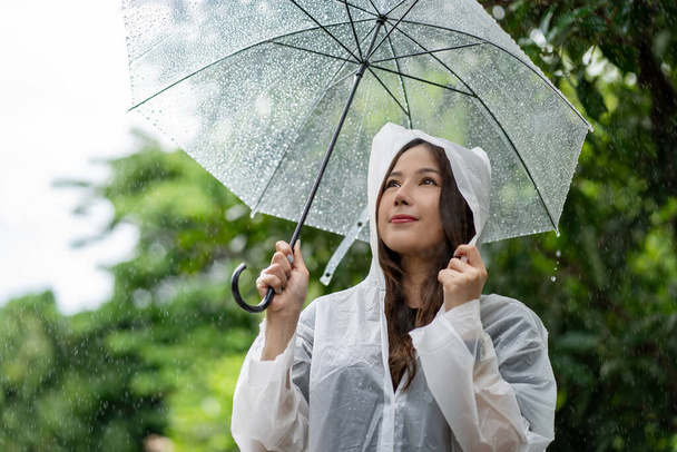 Тяжелый дождливый день. Счастливая азиатка в плаще и с зонтиком на улице. - Фото, изображение