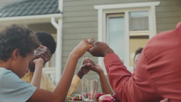 Vita alta della famiglia afroamericana che si tiene per mano e prega mentre pranziamo insieme all'aperto nel cortile durante la giornata estiva - Filmati, video