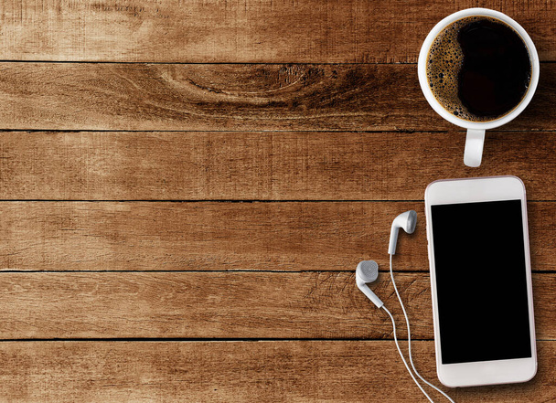 Top view Smart phone and earphone with cup of coffee on old wooden background with copy space. - Photo, Image