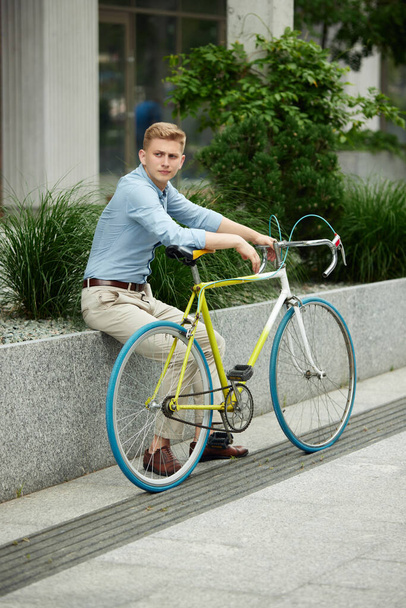 Businessman, office worker wearing stylish smart casual clothes, sitting on street, outside the office with bike. Urban background. Concept of business, active lifestyle, fashion, youth, ecology - Valokuva, kuva