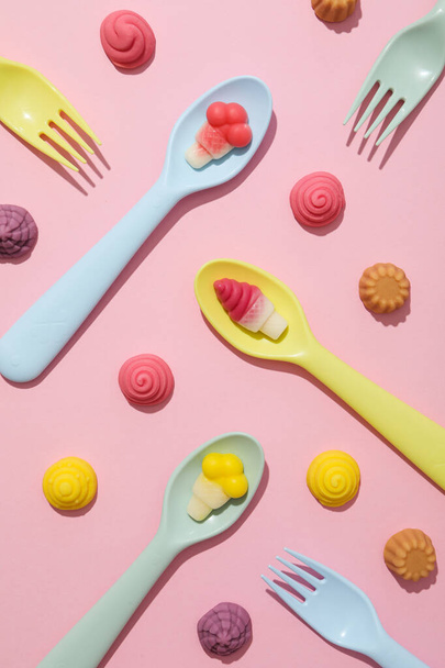 Caramelos de gelatina en cucharas, tenedores sobre fondo rosa, vista superior - Foto, imagen