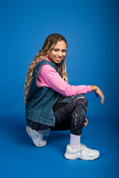 happy african american woman with dreadlocks posing on blue background, sporty outfit, smile - Fotoğraf, Görsel