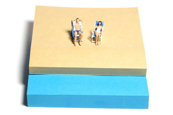 Personajes creativos miniatura juguete figura fotografía. Instalación de notas adhesivas. Una pareja relajándose en el banco de la playa. Aislado sobre fondo blanco. Foto de imagen - Foto, imagen
