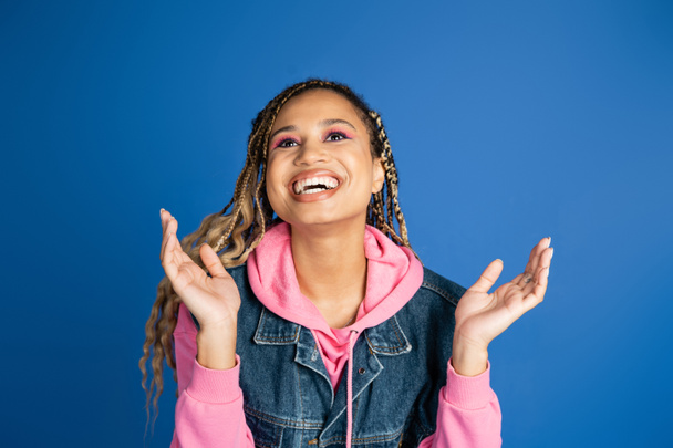 heureuse femme afro-américaine avec dreadlocks rire et geste sur fond bleu, positive - Photo, image