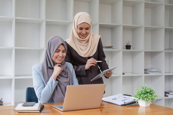 Young muslim female business worker discussing with friends sitting together, working with laptop and financial documents at desk. - Foto, Imagem