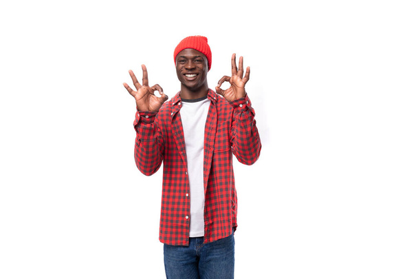glatte junge afrikanische Mann in kariertem Hemd mit Handbewegung über isolierten weißen Hintergrund. - Foto, Bild
