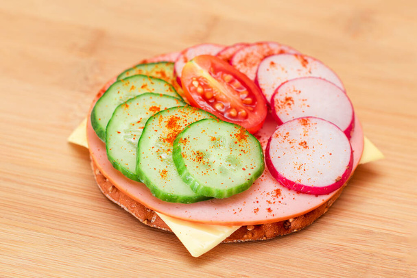 Crispy Cracker Sandwich with Fresh Cucumber, Cheese, Sausage, Radish and Tomato on Cutting Board. Easy Breakfast. Quick and Healthy Sandwiches. Crispbread with Tasty Filling. Healthy Dietary Snack - 写真・画像