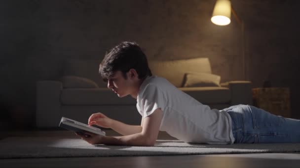 Adolescent mignon lisant un livre la nuit dans le salon. Apprentissage des étudiants à domicile - Séquence, vidéo