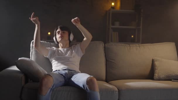 Teini-ikäinen poika kuuntelee rentouttavaa musiikkia istuu sohvalla yöllä. - Materiaali, video