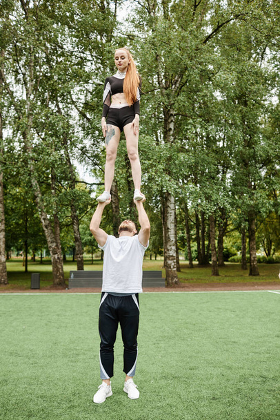 Vertical image of young girl from cheerleading team doing trick together with man outdoors - Fotografie, Obrázek