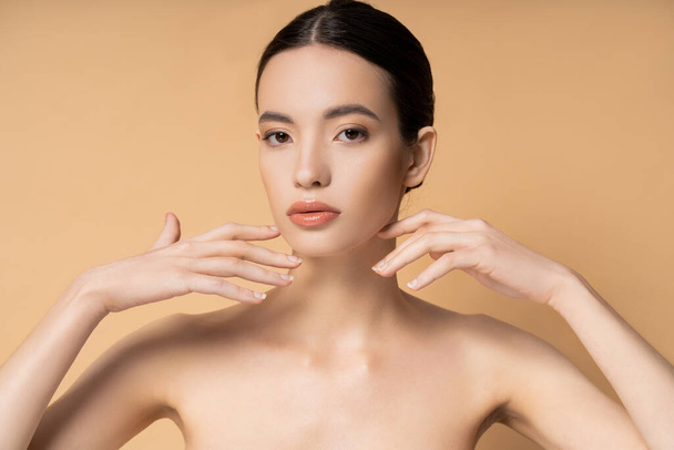 Young asian woman with natural makeup touching face and looking at camera isolated on beige - Φωτογραφία, εικόνα
