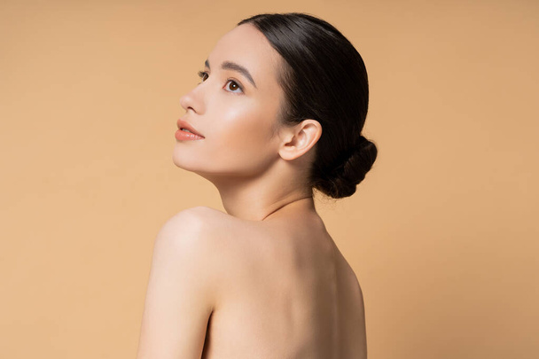 Giovane e bella donna asiatica con pelle perfetta e spalle nude in piedi isolate sul beige - Foto, immagini