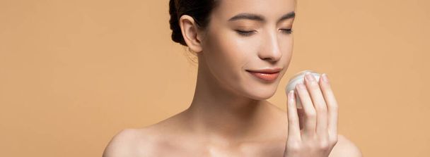 Young asian woman with naked shoulders smelling cosmetic cream isolated on beige, banner - Φωτογραφία, εικόνα