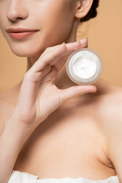 Cropped view of young woman in top holding cosmetic cream and standing isolated on beige - Photo, Image