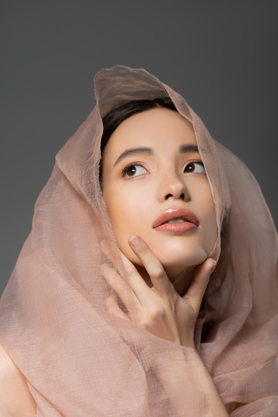 Portrait de jeune femme asiatique au visage naturel posant avec un tissu beige isolé sur gris - Photo, image