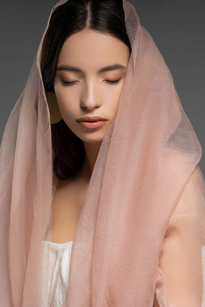 Pretty young asian woman with closed eyes posing in beige cloth and standing isolated on grey - Fotoğraf, Görsel