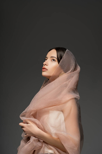 Jolie jeune modèle asiatique avec maquillage quotidien et tissu beige posant isolé sur gris - Photo, image
