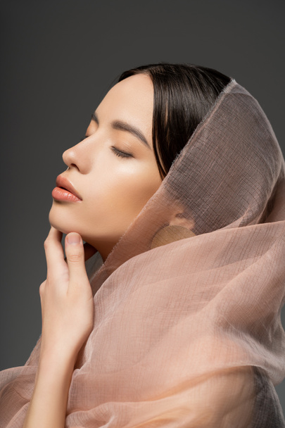 Portrait of attractive young asian woman with beige cloth posing with closed eyes isolated on beige - Photo, Image