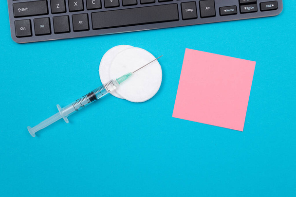 Vaccination, Immunology or Revaccination Concept - A Medical Disposable Syringe Lying on Blue Table in Doctors Office in a Hospital or Clinic. Blank Pink Sticky Note - Mock Up with Copy Space - Photo, image