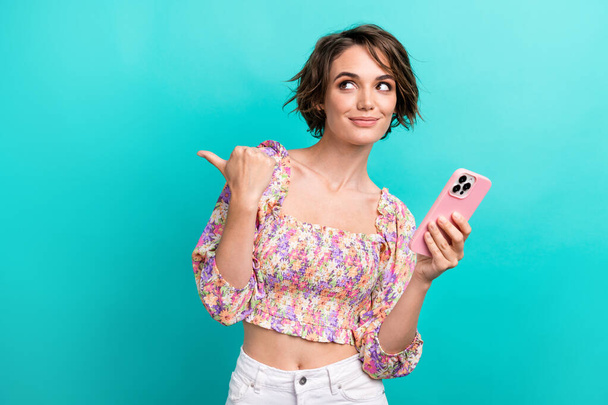 Photo of good mood nice woman wear colorful dress directing look empty space hold smartphone isolated on turquoise color background. - Foto, imagen