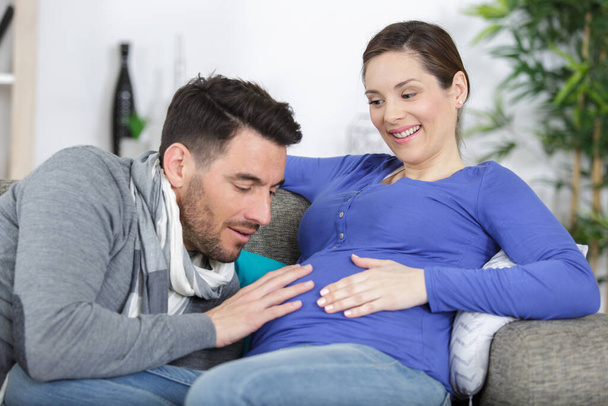 handsome man is listening to his beautiful pregnant wifes tummy - Photo, image