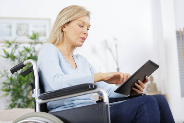 mujer madura feliz en silla de ruedas utilizando asistencia interent - Foto, imagen