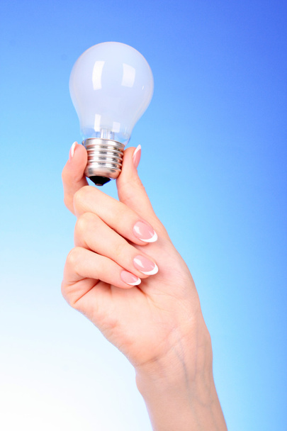 Hand with lightbulb on blue background - Φωτογραφία, εικόνα