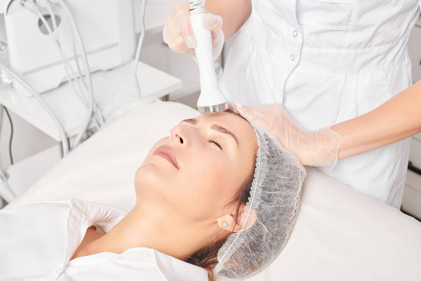 Cosmetologist makes ultrasound skin tightening for rejuvenation woman face using phonophoresis, anti aging cosmetic procedure with in beauty spa salon. Beautician makes ultrasonic skincare lifting - Photo, Image