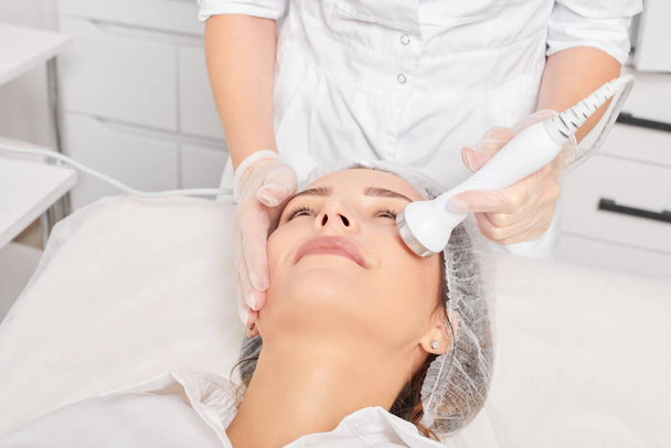 Cosmetologist makes ultrasound skin tightening for rejuvenation woman face using phonophoresis, anti aging cosmetic procedure with in beauty spa salon. Beautician makes ultrasonic skincare lifting - Photo, Image