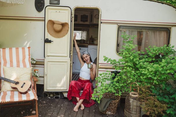 Šťastná hippie dívka se dobře baví s šálkem čaje v přívěsu karavanu. Dovolená, dovolená, výlet koncept.Vysoká kvalita fotografie - Fotografie, Obrázek