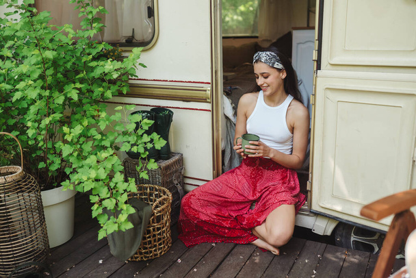 Chica hippie feliz se están divirtiendo con la taza de té en caravana remolque. Vacaciones, vacaciones, concepto de viaje.Foto de alta calidad - Foto, imagen