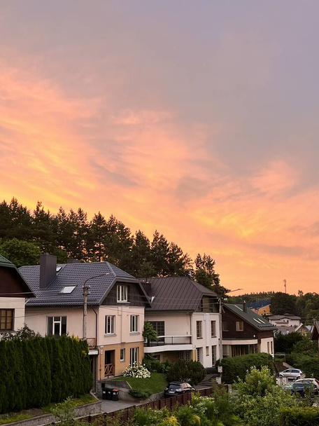 Zachód słońca w miejscowości z widokiem na europejskie domy i las. Nowoczesne domy prywatne. Życie w środku natury - Zdjęcie, obraz