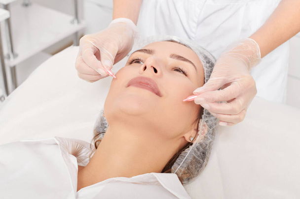 Kosmetologe trägt Gesichtsöl-Kapseln auf das Gesicht der Frau zur Verjüngung, Anti-Aging-kosmetische Verfahren in Beauty-Spa-Salon. Kosmetikerin hält Ölkapseln in Handschuhen zur Ernährung - Foto, Bild