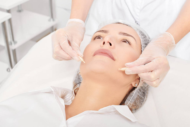 Beautician applies facial oil capsules on woman face for rejuvenation, anti aging cosmetic procedure in beauty spa salon. Cosmetologist hands in gloves holds oil capsules for nourishment - Photo, Image