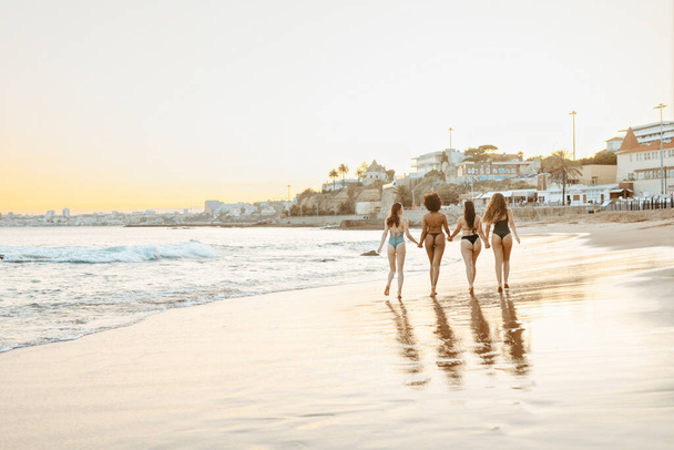 Πλάτη άποψη των τεσσάρων νεαρών γυναικών φίλους περπάτημα, κρατώντας τα χέρια και απολαμβάνοντας το καλοκαίρι στην παραλία κατά το ηλιοβασίλεμα, full length shot, δωρεάν χώρο αντίγραφο, banner - Φωτογραφία, εικόνα