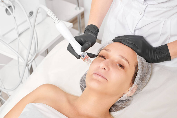 Kosmetolog sprawia, że aqua złuszczanie do odmładzania kobiety pielęgnacji twarzy, anti aging zabiegu kosmetycznego w salonie spa uroda. Ręce kosmetyczki w czarnych rękawiczkach sprawia, że leczenie skóry twarzy do zaciskania - Zdjęcie, obraz