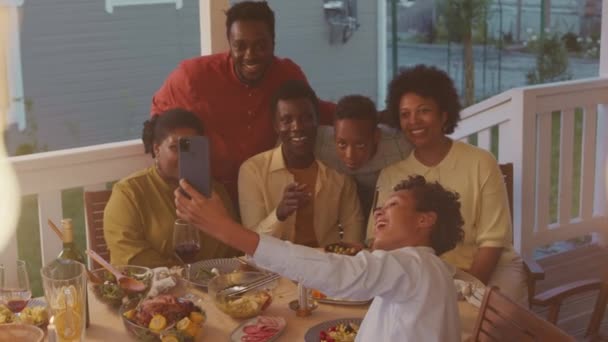 Big African American family taking selfie portrait on smartphone during dinner on porch of their house on warm summer evening - Imágenes, Vídeo