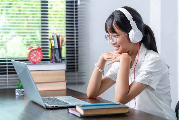 Boldog mosolygó női diák fülhallgatót visel beszél az online megbeszélés segítségével laptop otthoni irodában. női főiskolai hallgató tanul távoktatás üzleti - Fotó, kép