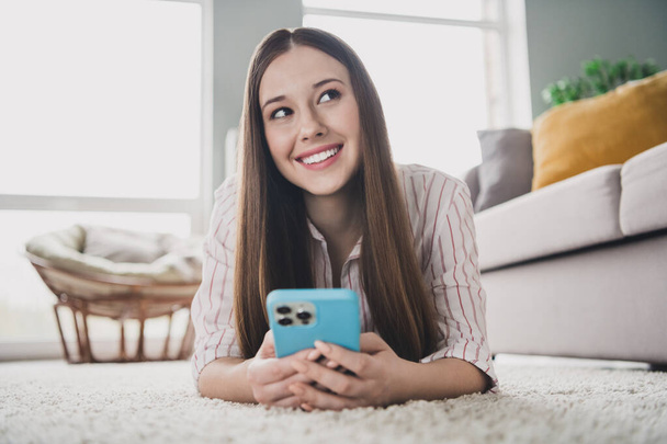 Photo of adorable dreamy young girl wear striped shirt lying floor online order modern gadget indoors apartment room. - Φωτογραφία, εικόνα