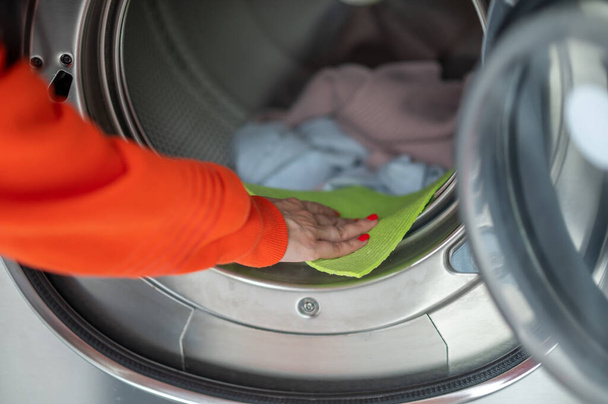 Public laundry. Unrecognizable woman washing dirty clothes, cleaning washing machine with rag in the laundry room. - 写真・画像