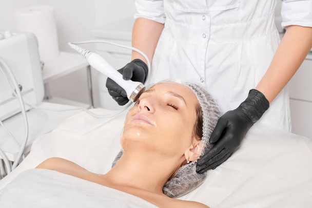Kosmetolog sprawia, że ultradźwiękowe napięcie skóry do odmładzania twarzy kobiety przy użyciu fonoforezy, zabieg kosmetyczny anti aging z w salonie piękności spa. Kosmetyk sprawia, że ultradźwiękowe podnoszenie skóry - Zdjęcie, obraz