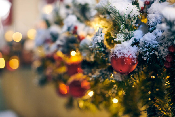 Sarı çelenklerle süslenmiş Noel ağacı ampulleri karla kaplı, açık havada ksenli yeşil ağaç dekoratif kırmızı ampuller, açık havada kış tatili atmosferi. Süslemeleri ve çelenkleri olan Noel ağacı - Fotoğraf, Görsel