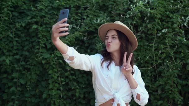 Young beautiful girl take selfie from hands with phone on summer city street on green background. Urban life concept. - Video, Çekim